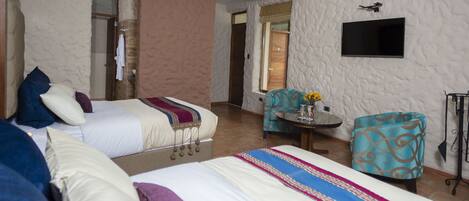 A hotel room with two beds, a TV mounted on the wall, a small table with a vase of flowers, and a patterned armchair.