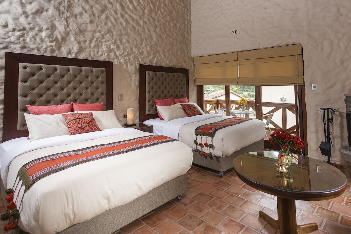 Quarto com duas camas, uma mesinha com um vaso e vista para o exterior.