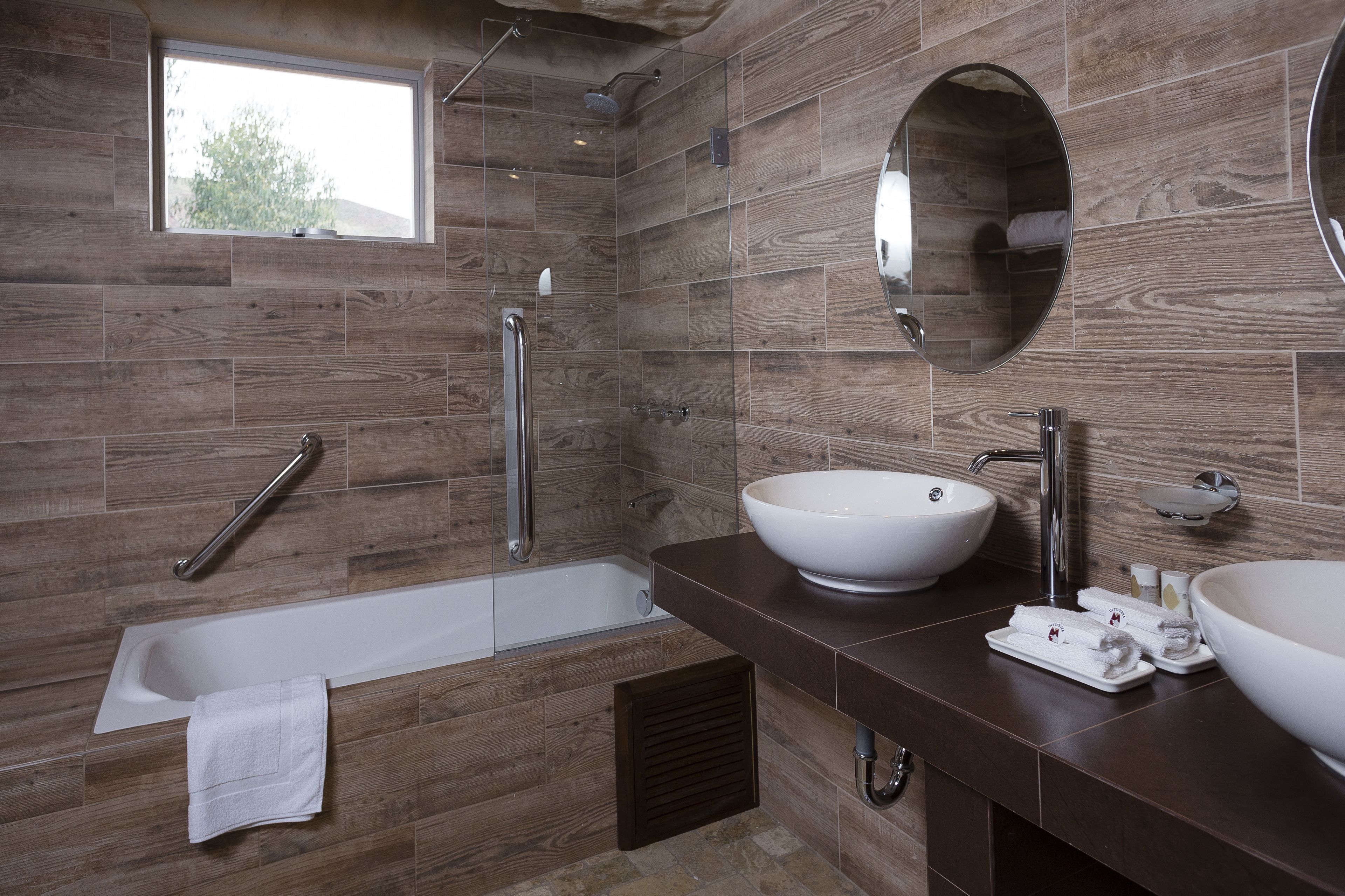 A modern bathroom with a bathtub, two sinks, a window, and a shower.