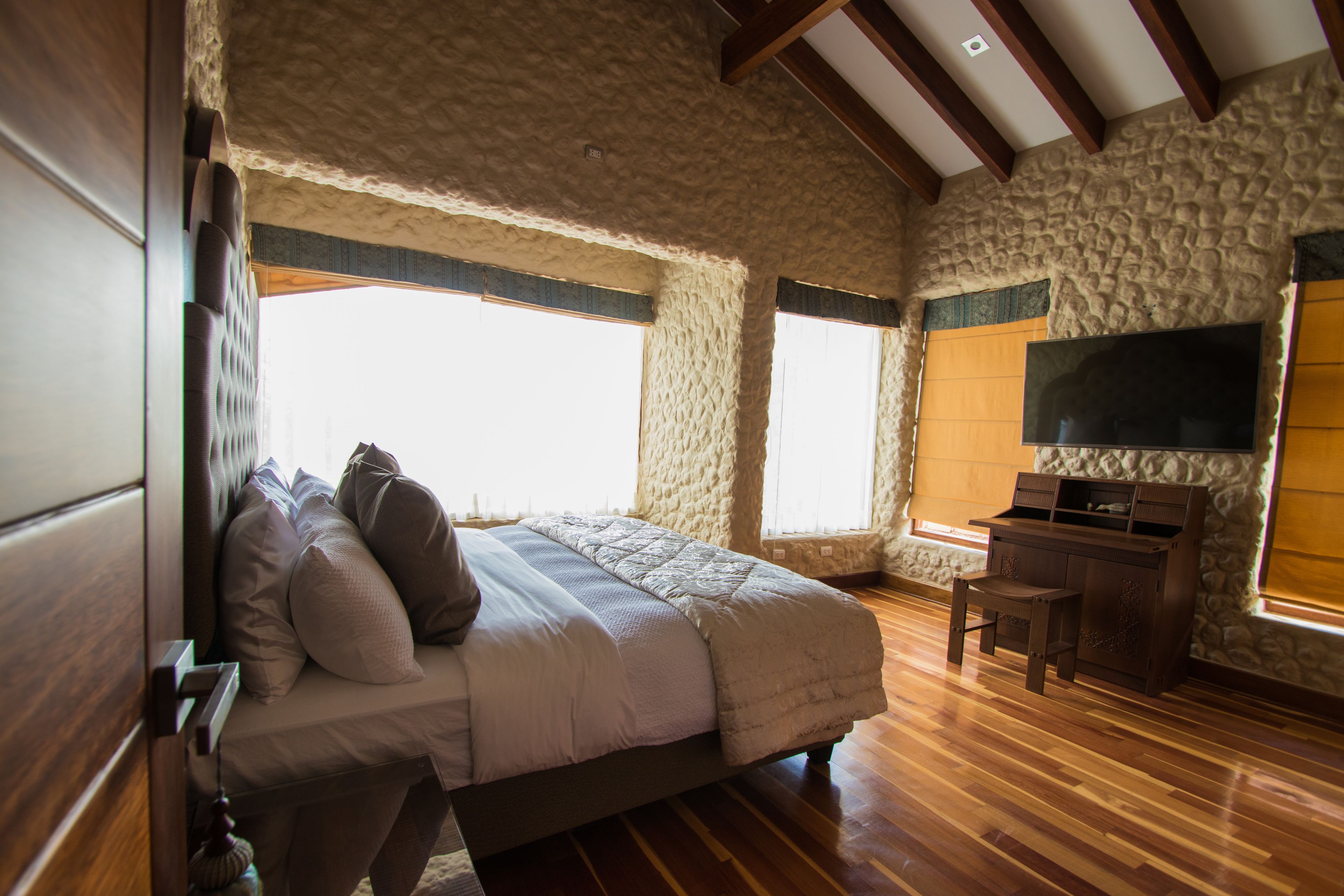 Une chambre à coucher avec un lit, un bureau en bois, des murs en pierre et un téléviseur.