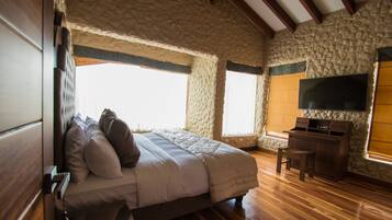 A bedroom with a bed, wooden desk, stone walls, and a TV.