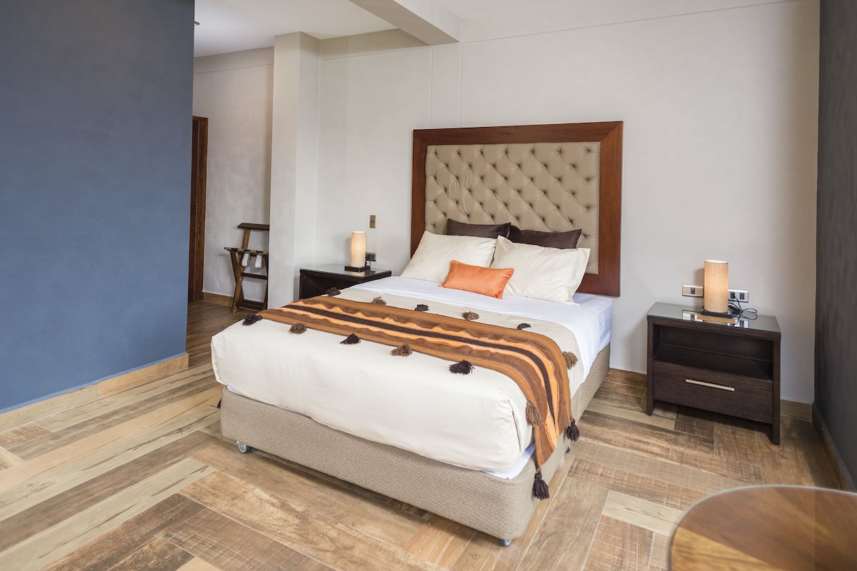 Quarto com uma cama grande, cabeceira de madeira, duas mesas de cabeceira e um criado-mudo.