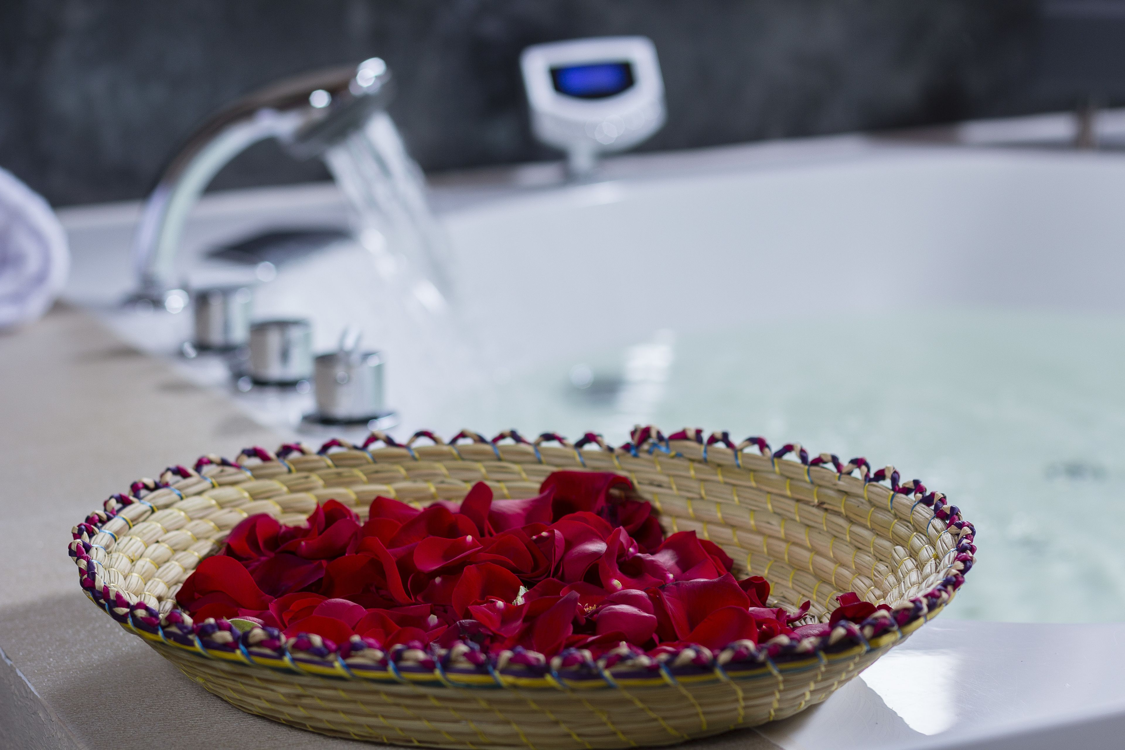 A bathroom with a sink, a small digital display, and a woven basket filled with red rose petals.