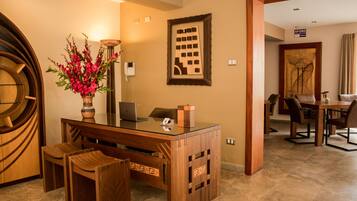 A hotel reception area with a wooden desk, chairs, a vase of flowers, a framed artwork, and a sign reading "AFORO".