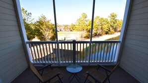 A balcony with two chairs and a table, overlooking a wooded area and a body of water. - Ironwood Apartment 1722 (North Myrtle Beach)