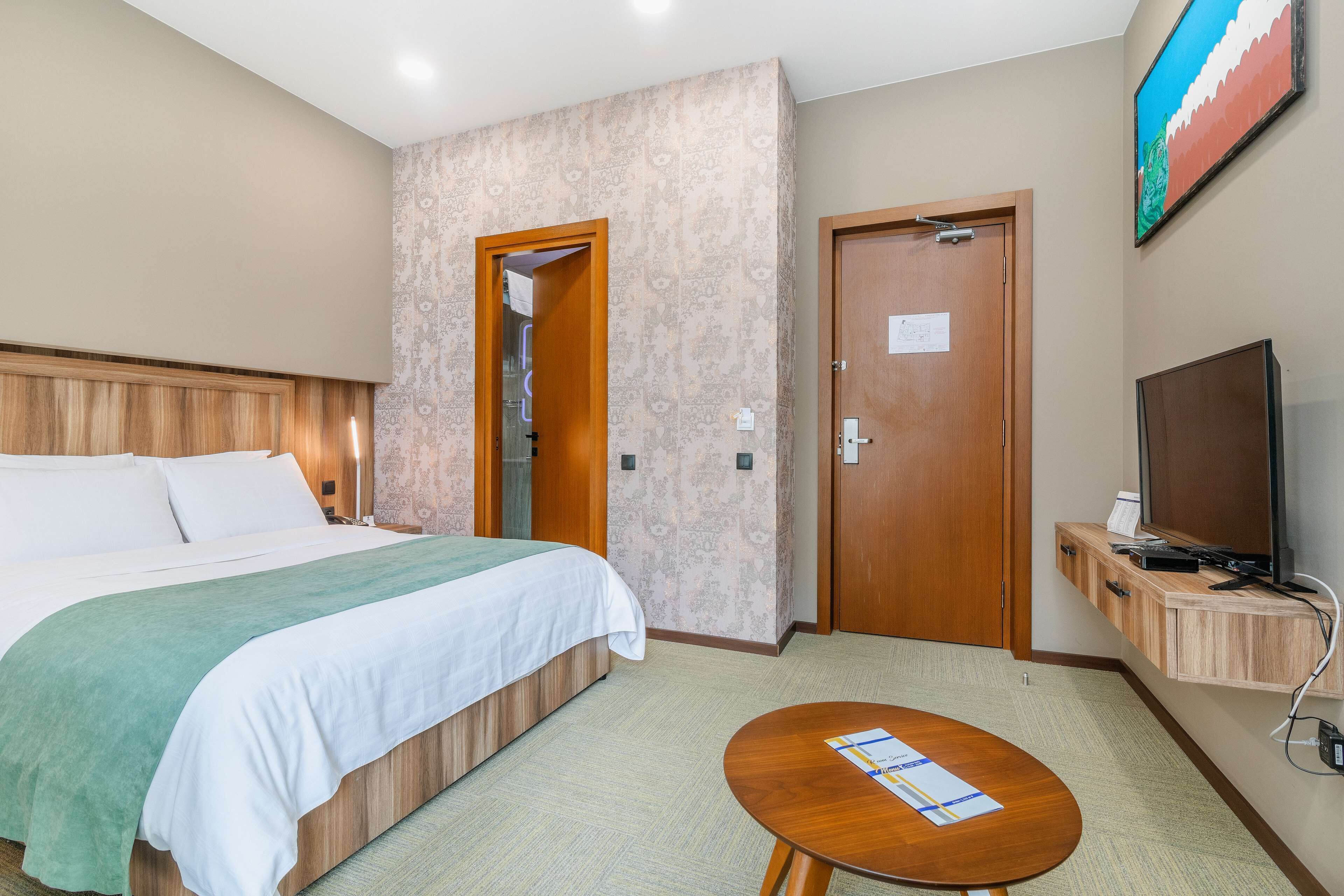 A hotel room with a bed, a desk, a television, and a door.