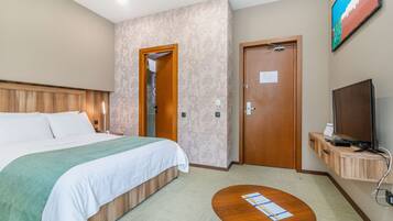A hotel room with a bed, a desk, a television, and a door.