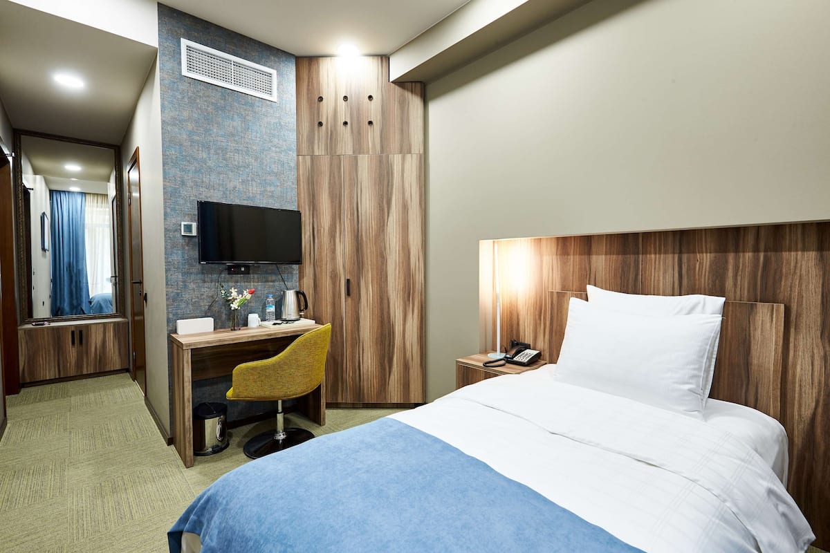 Ein Hotelzimmer mit Bett, Schreibtisch mit Stuhl, Fernseher, Nachttisch mit Telefon und Kleiderschrank.