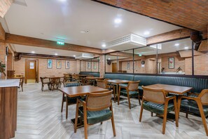 A restaurant with wooden tables and green cushioned booths, brick walls, and a herringbone floor pattern.