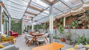 Un vaste espace intérieur doté d’un plafond en verre, de meubles en bois et de diverses plantes en pot.