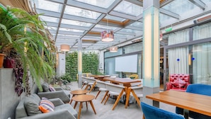 Un espace intérieur moderne doté d’un plafond en verre, de tables en bois, de canapés gris et de chaises bleues.