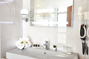 A bathroom with a white sink, a mirror, a towel rack, a hairdryer, and a small potted plant.