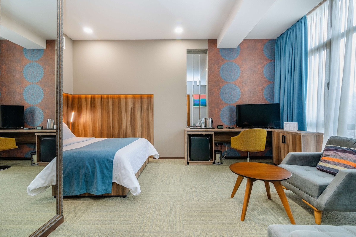 Una habitación de hotel con una cama, un escritorio con ordenador, televisor, sofá y espejo.