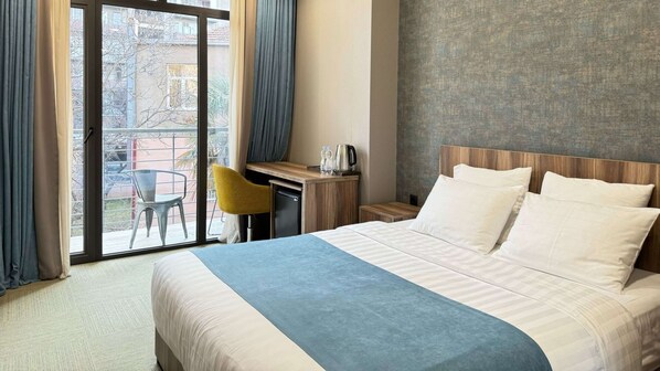 A hotel room with a bed, a desk, a chair, and a view of the outside. - Best Western Tbilisi City Center (Tbilisi)