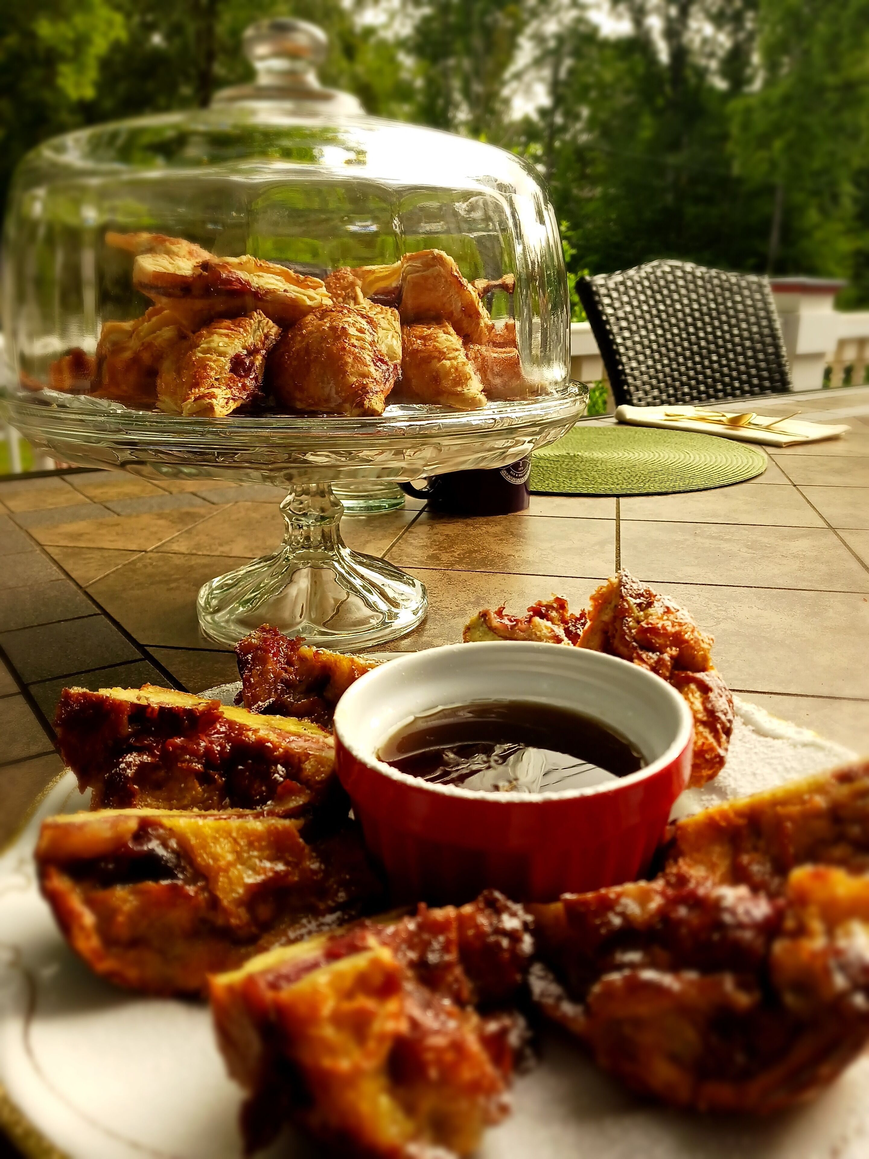 Un présentoir à desserts en verre, contenant divers pâtisseries, et un bol de sauce pour tremper, le tout posé sur une table.