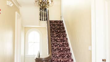 A grand staircase with a floral carpet, a chandelier, and a white door.