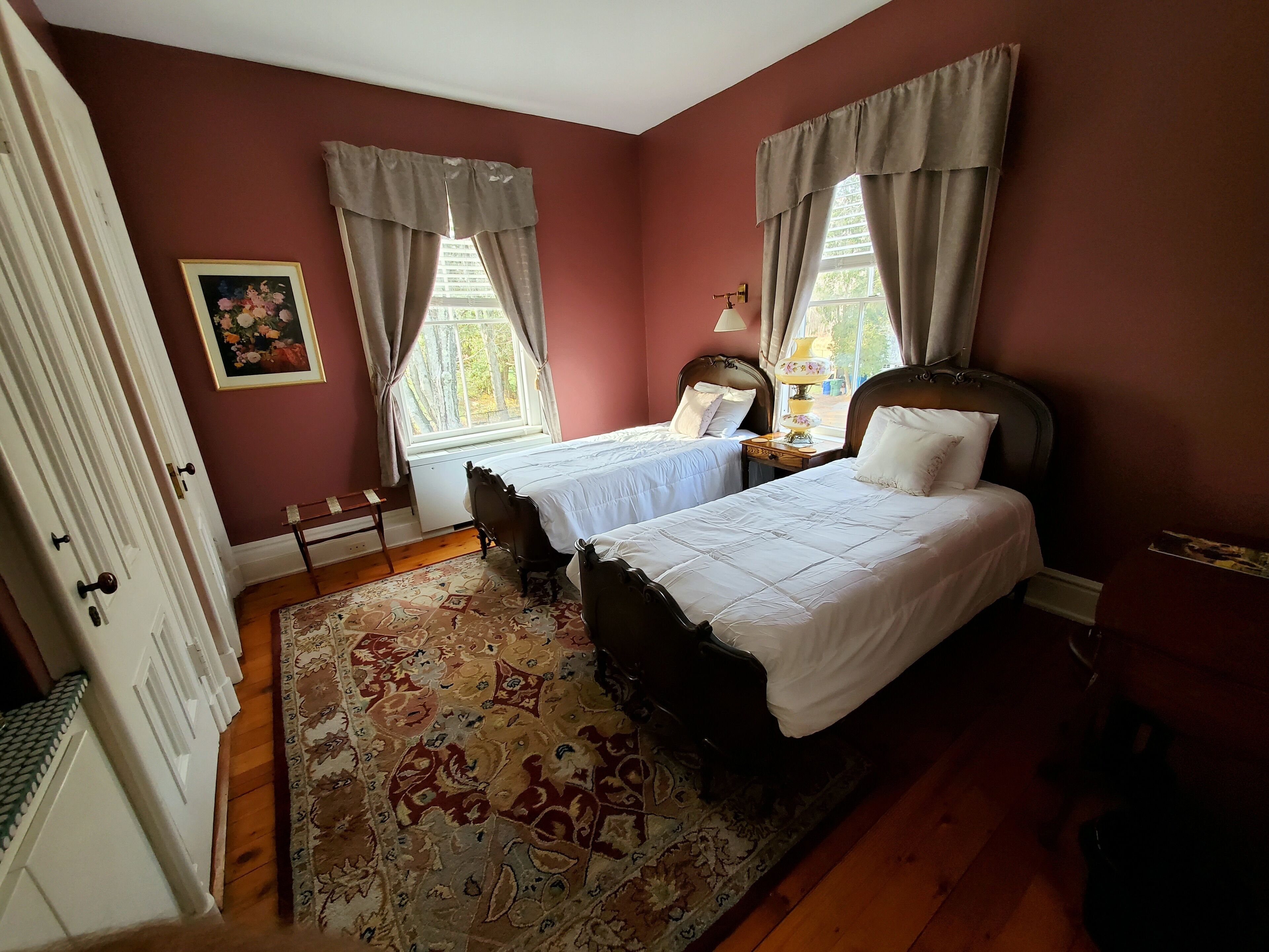 A bedroom with two beds, a wooden floor, a patterned rug, and a painting on the wall.