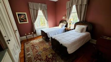 A bedroom with two beds, a wooden floor, a patterned rug, and a painting on the wall.