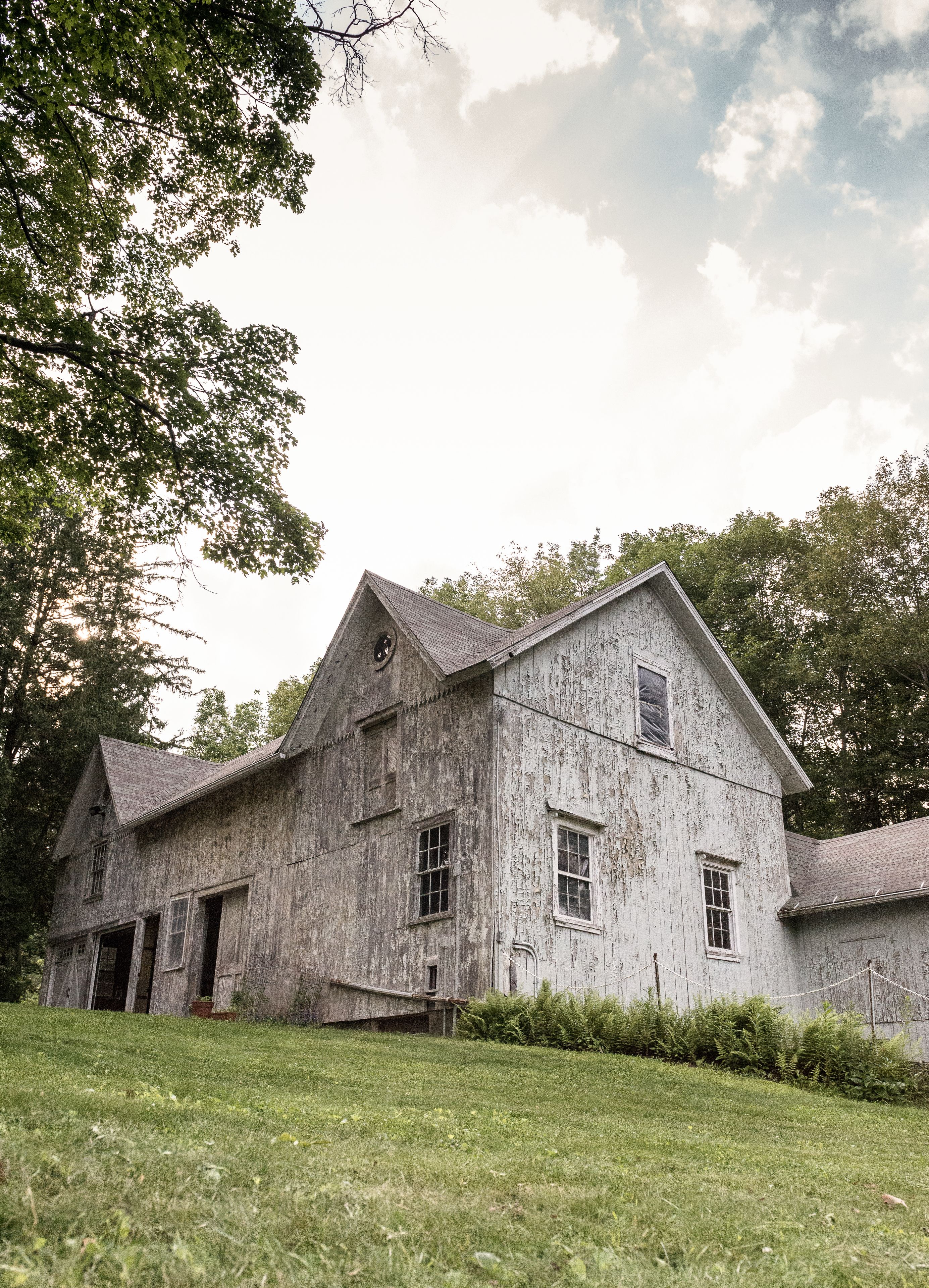 A large, rustic wooden building with multiple windows and a sloped roof, surrounded by lush greenery.