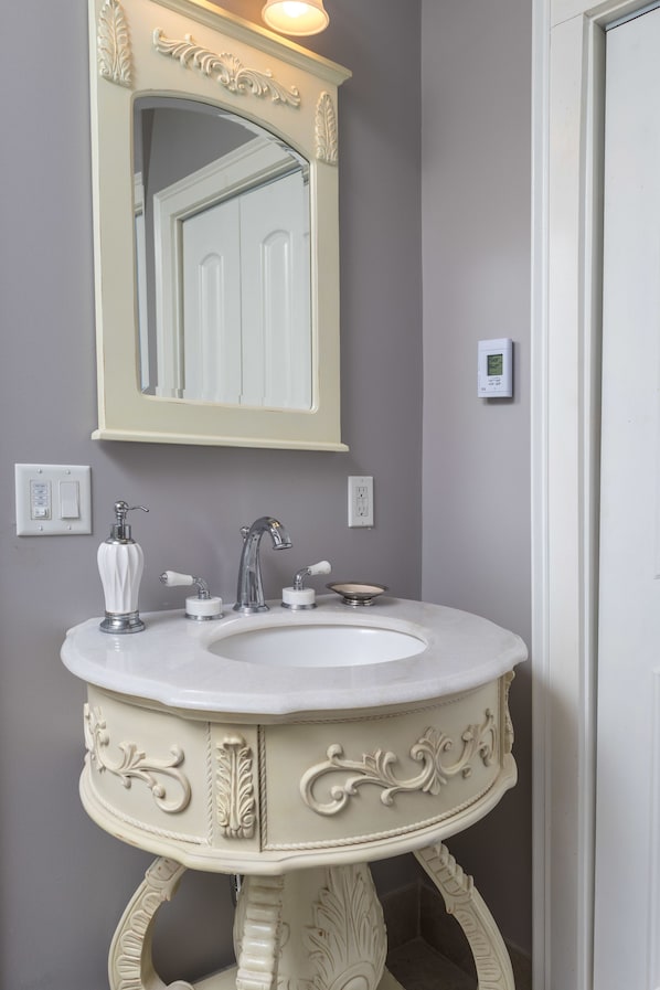 A bathroom with a white vanity, a mirror above the sink, and a light switch on the wall. - The Bevin House Bed & Breakfast (East Hampton)