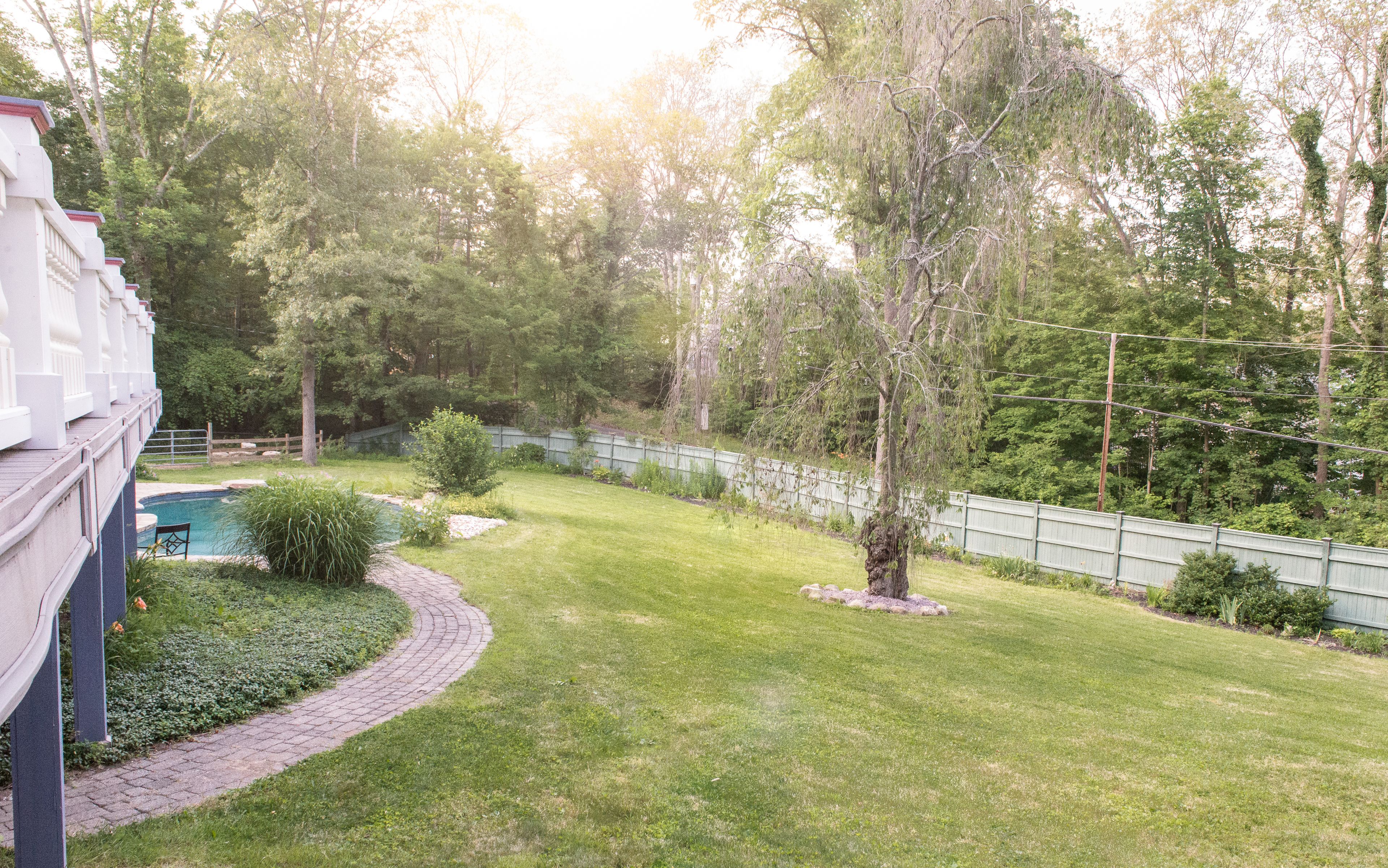 A backyard with a swimming pool, a wooden deck, and a stone pathway.