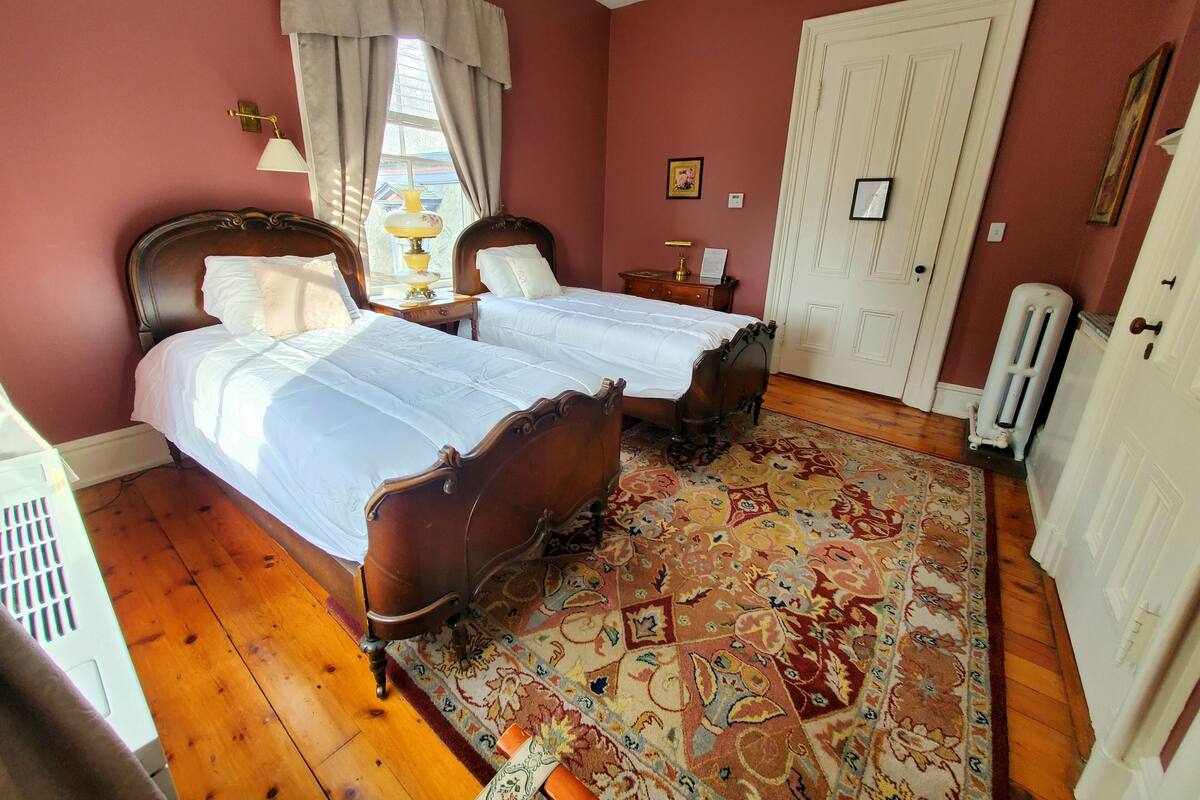A bedroom with two wooden beds, a patterned rug, a white radiator, and a door.