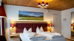 Hotelkamer met een groot bed, twee bedlampen, een vastgeplakt landschap en een houten plafond.