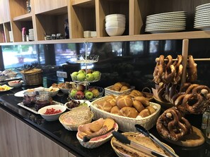 Un buffet proposant une variété de plats, notamment des fruits, du pain et des pâtisseries.