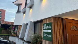 Een hotel met een wit gevel, houten balkons met bloemen, en een bord dat een receptie aangeeft.