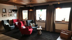 Een gezellige zithoek met een zwart tapijt, houten vloeren en een mix van rode en grijze fauteuils.