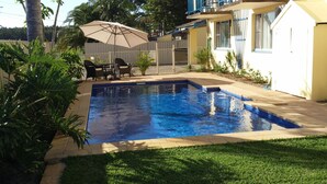 Une piscine dont le bord est revêtu de carrelage, entourée d’une pelouse verdoyante et de palmiers.