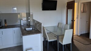 Une cuisine compacte avec un coin repas, un téléviseur à écran plat fixé au mur et une porte donnant sur une autre pièce.