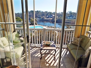 A balcony with a view of a lake and houses, furnished with a sofa and chairs, and a table with a bowl. - Edgewater Apartment 533 (North Myrtle Beach)