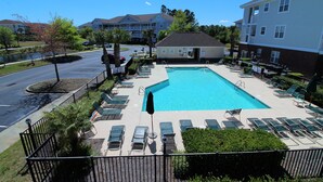 A swimming pool with lounge chairs, a covered area, and a view of surrounding buildings.