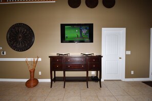 A room with a television mounted on the wall, a wooden desk, a white door, and a decorative wall piece.