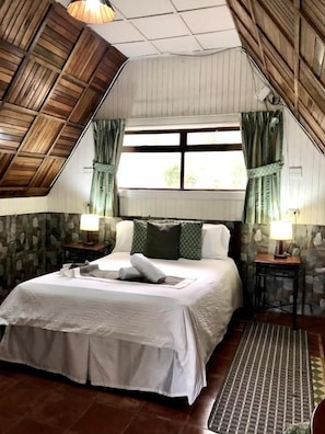 A bedroom with a sloped ceiling, a bed with white bedding, two bedside tables with lamps, and a window with curtains. - Hortensias Chalets Vara Blanca (Vara Blanca)