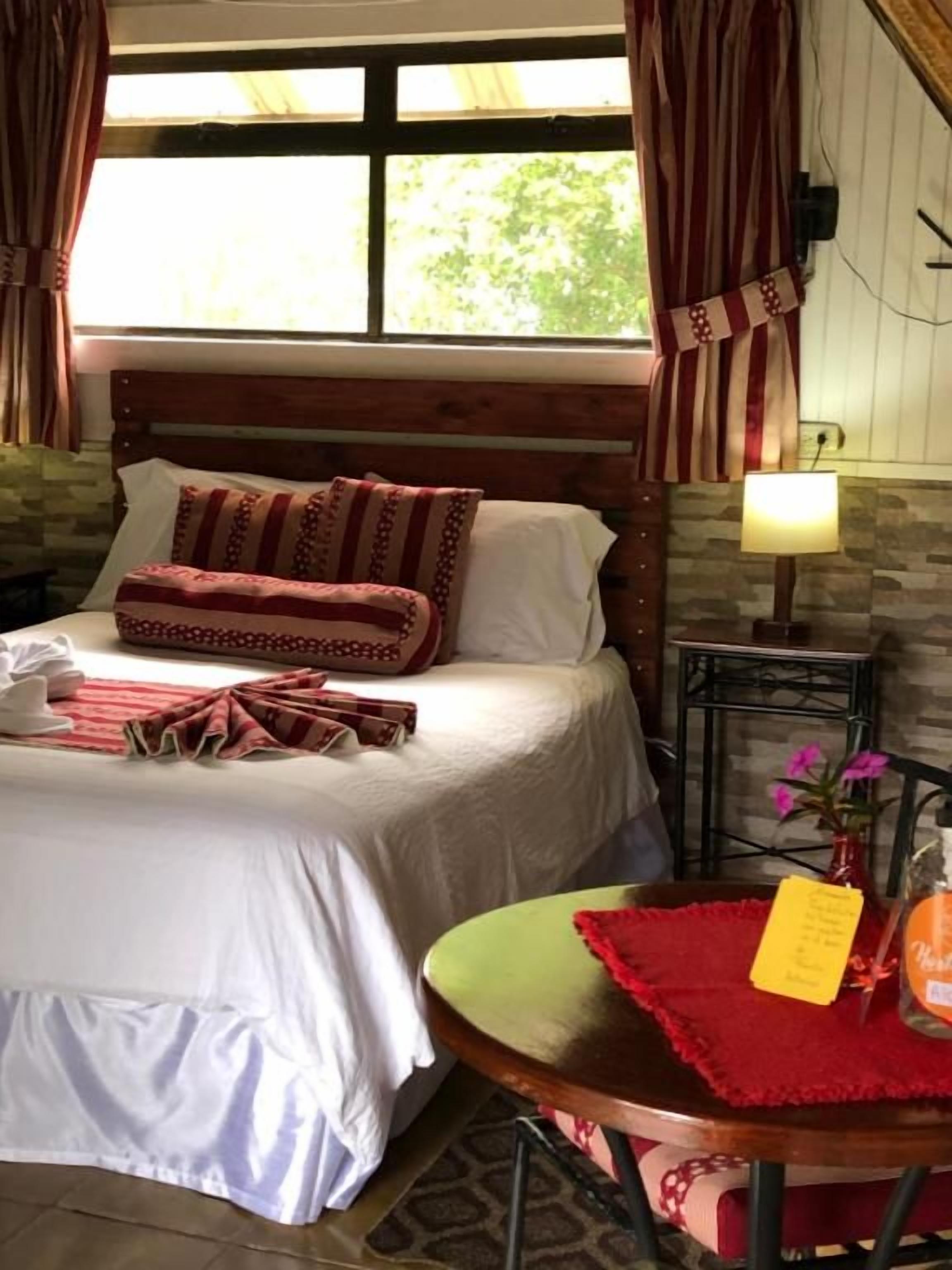 Une chambre à coucher avec un lit, une table de chevet avec une lampe, une chaise et une fenêtre avec des rideaux.