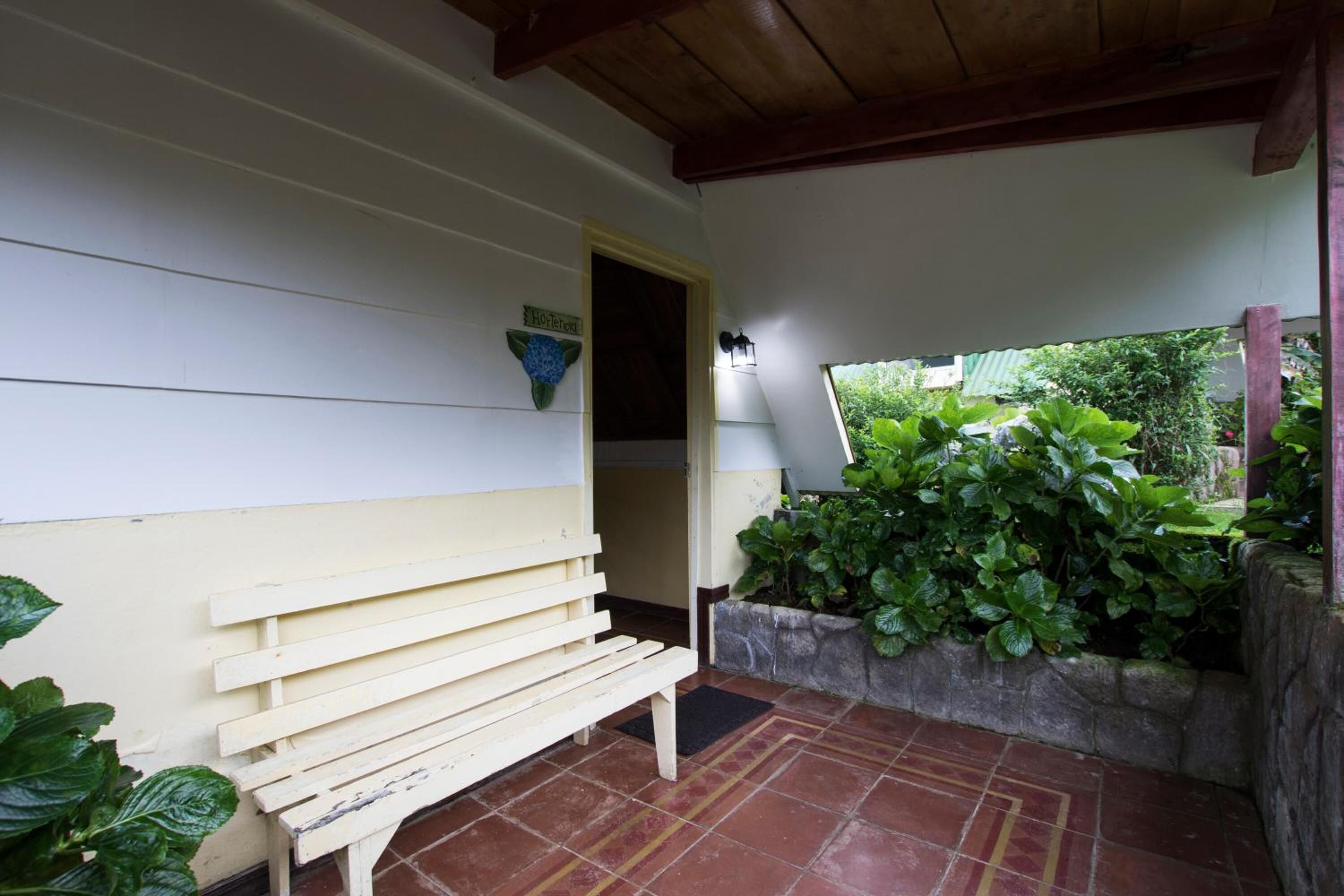 A covered outdoor seating area with a bench, a lamp, and a stone planter with greenery.