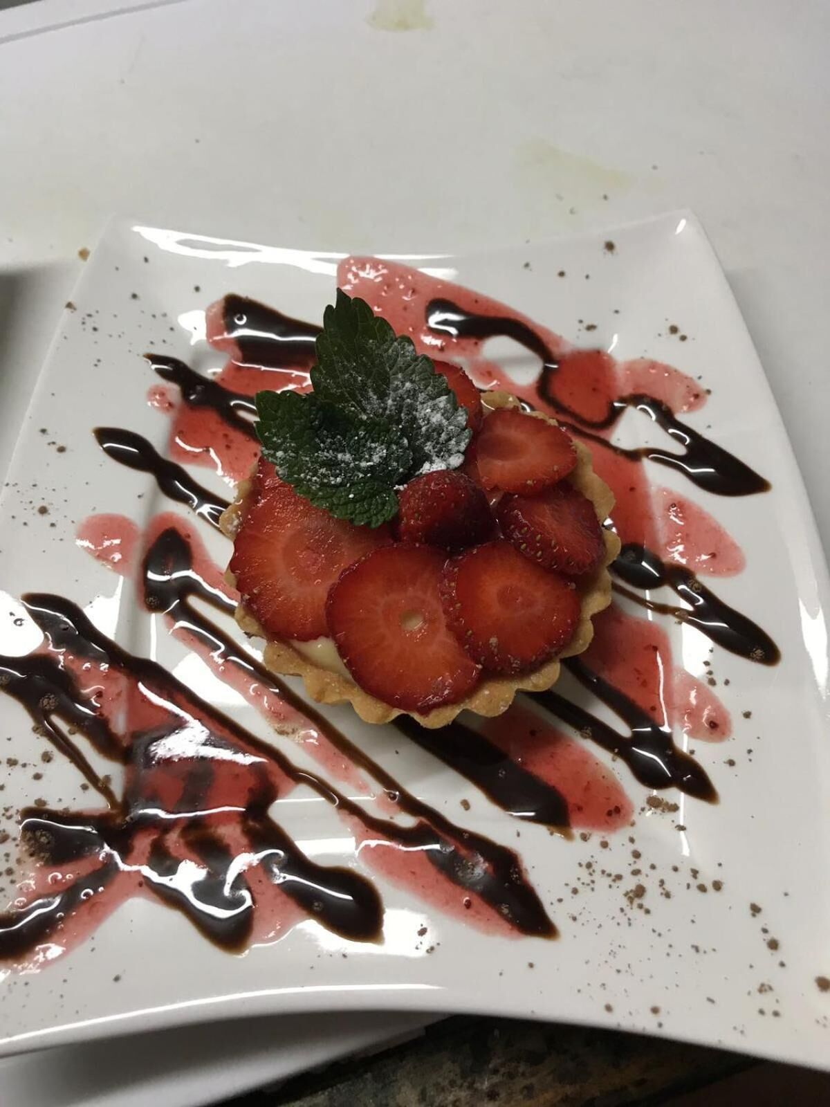 Un plato cuadrado con un postre de fresas y menta, rociado con salsa de chocolate.