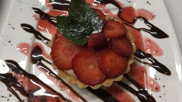 Un plato cuadrado con un postre de fresas y menta, rociado con salsa de chocolate.