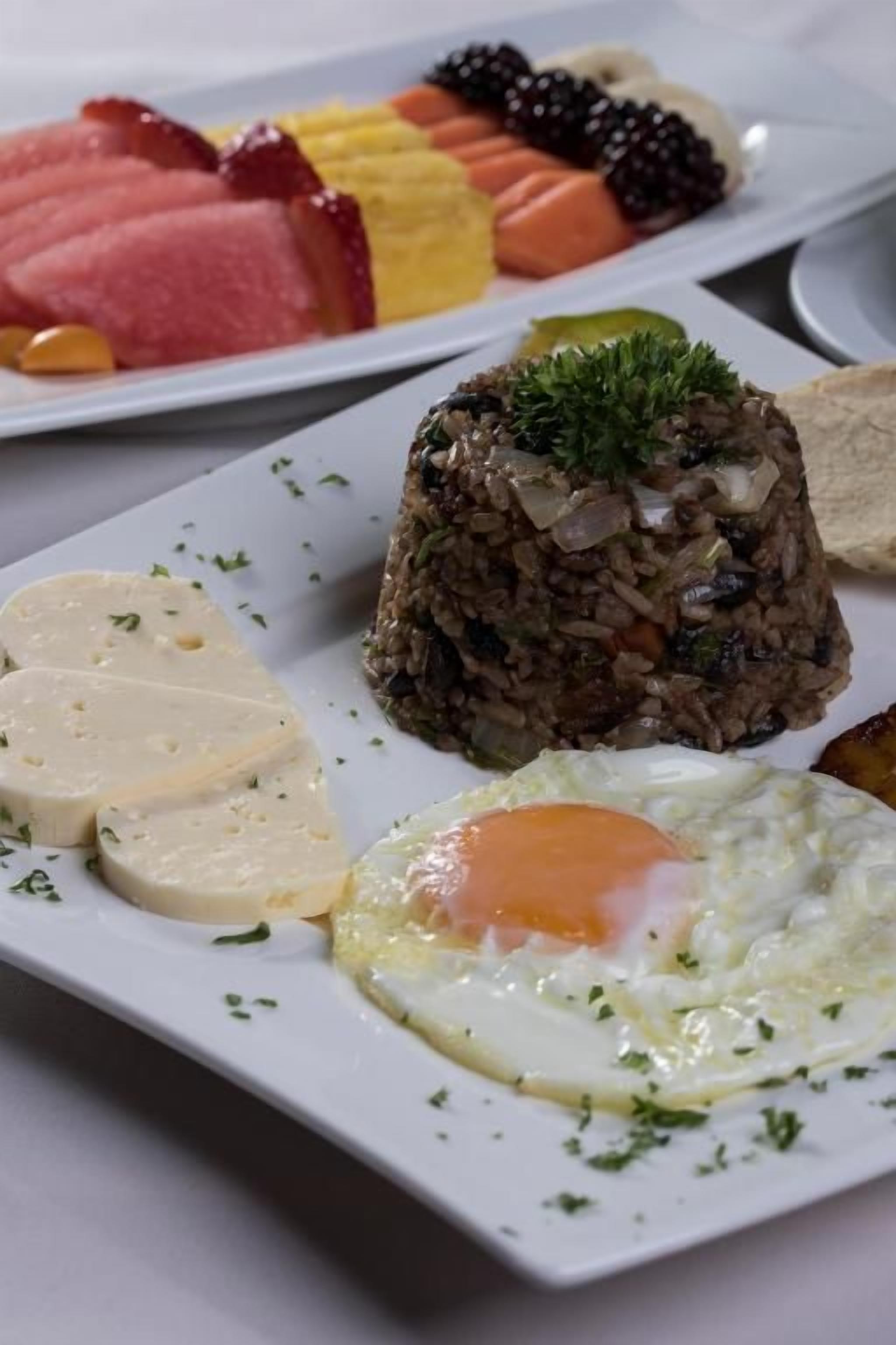 A plate with a variety of food items including a fried egg, slices of cheese, a meat dish, and a rice-based dish.