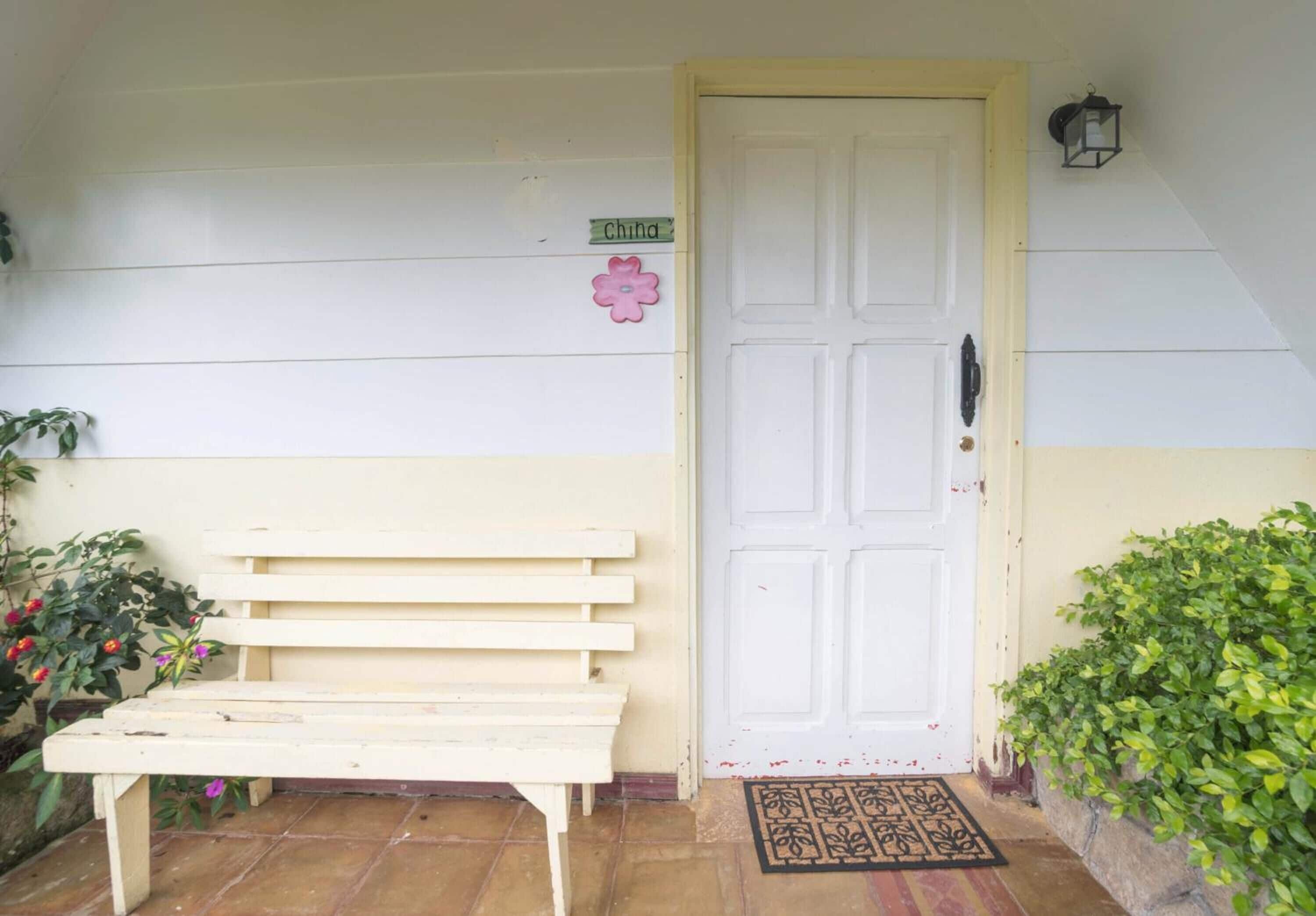 A white door with a small sign above it, a bench outside, and a potted plant to the right.