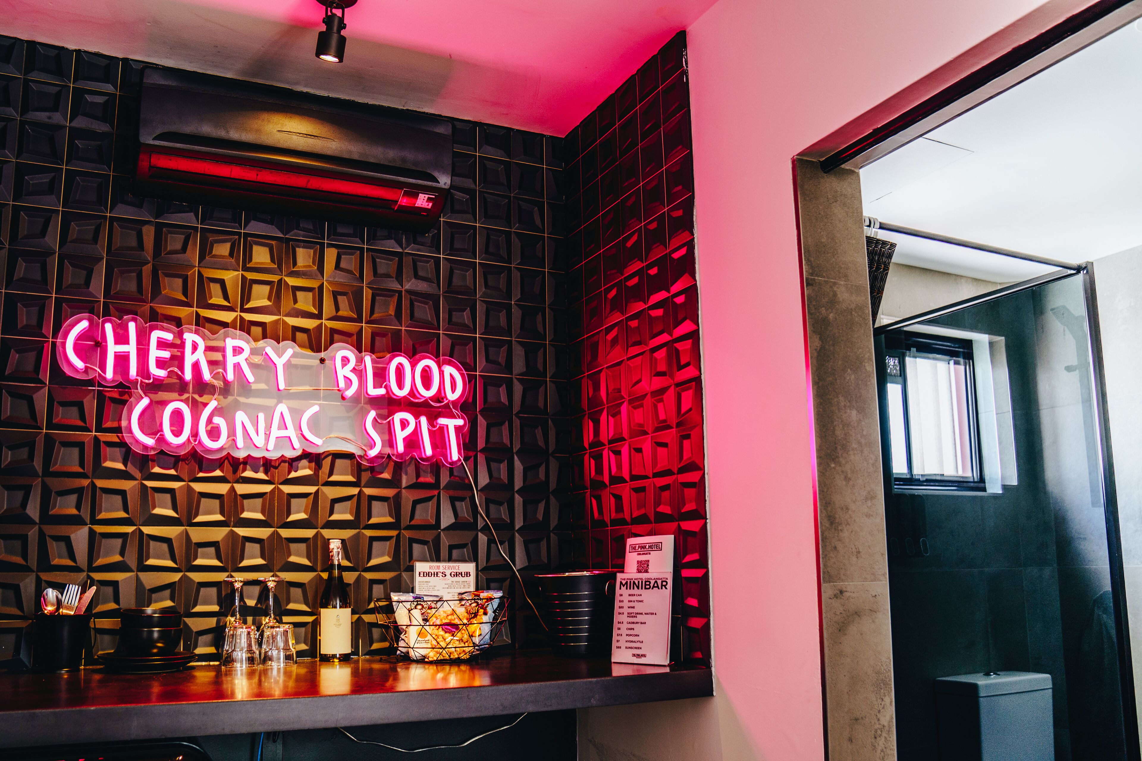 A bar area with a neon sign reading "CHERRY BLOOD COONAC SPIT".