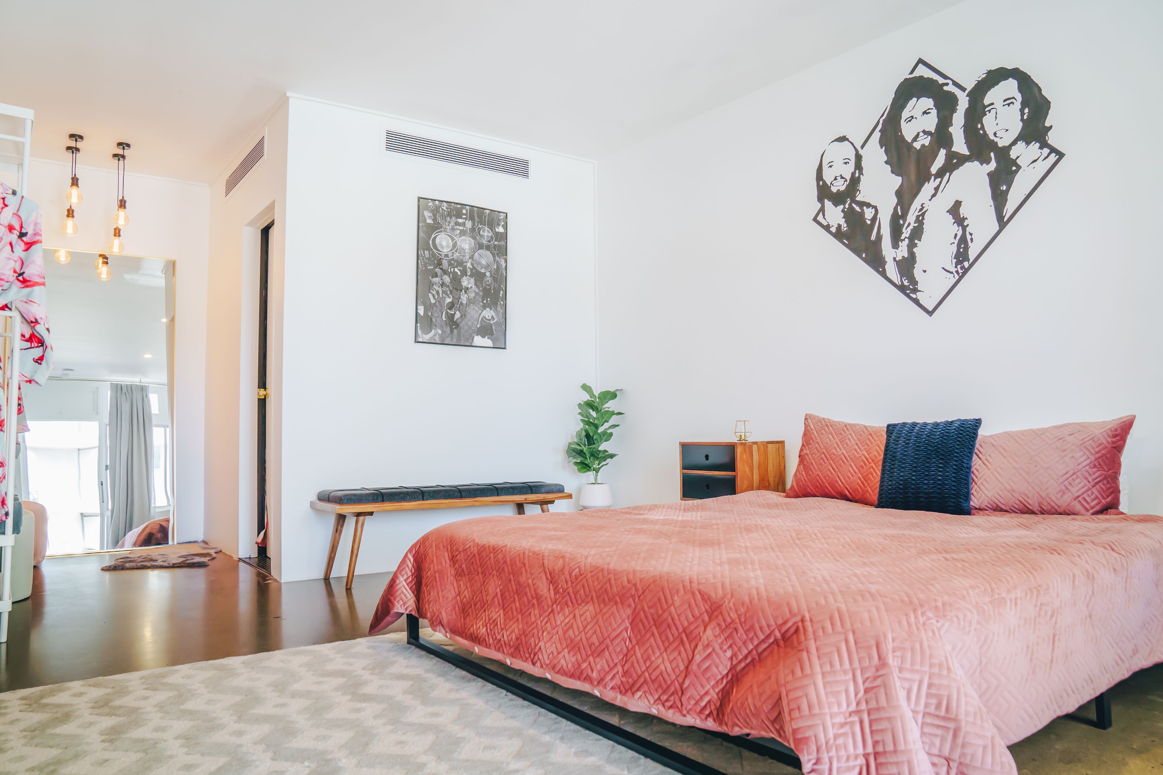 A bedroom with a large bed, a bedside table, a mirror, and a wall art piece.