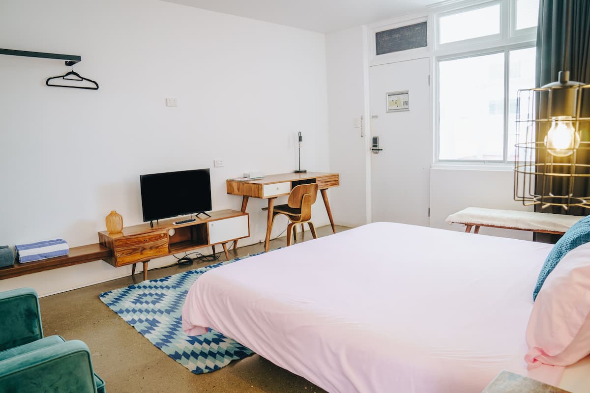 Een slaapkamer met een bed, bureau, stoel, televisie en een raam.