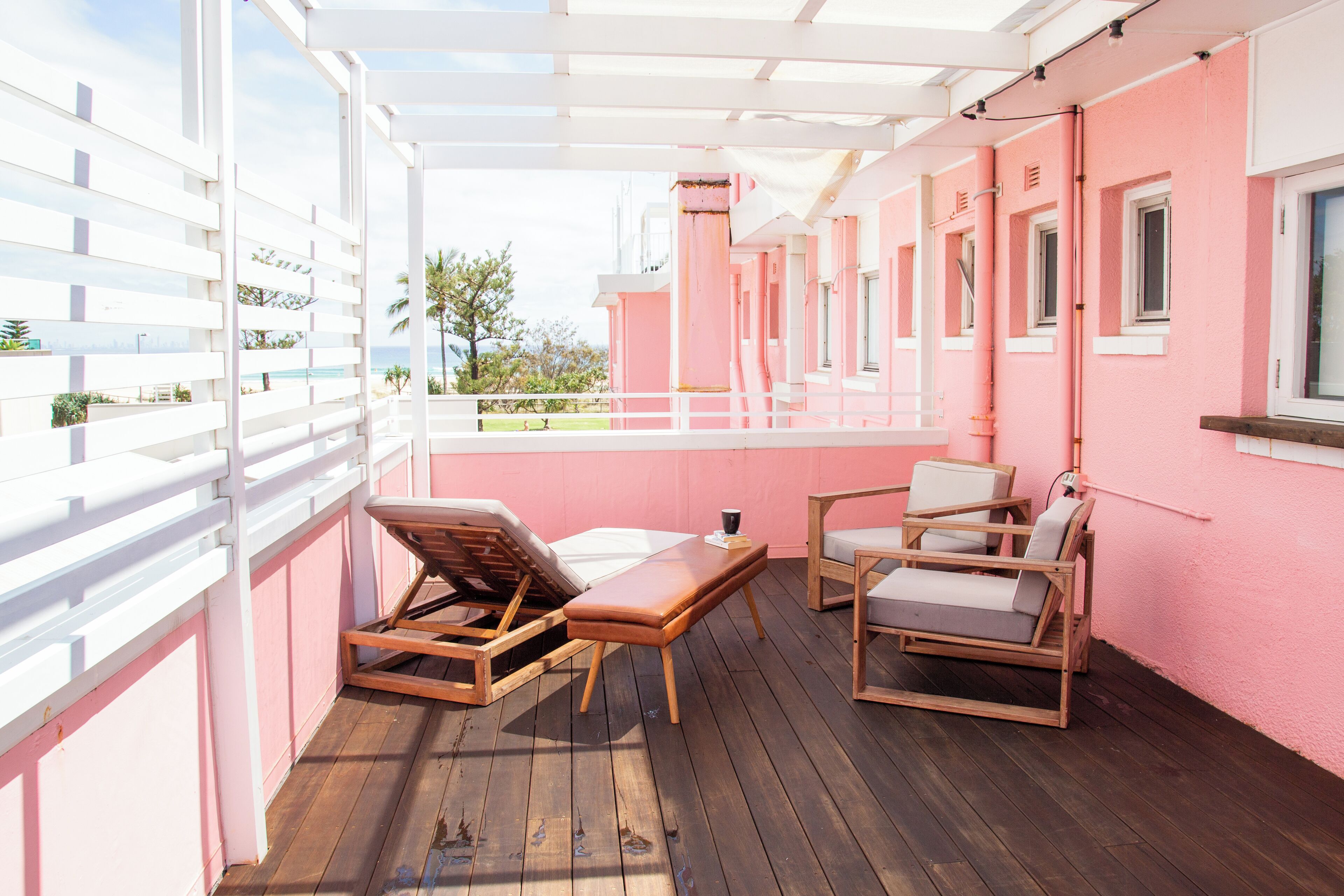 A pink building with a wooden deck, white railings, and outdoor seating.