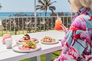 Een tafel met verschillende gerechten en een drankje, op een balkon met uitzicht op zee.