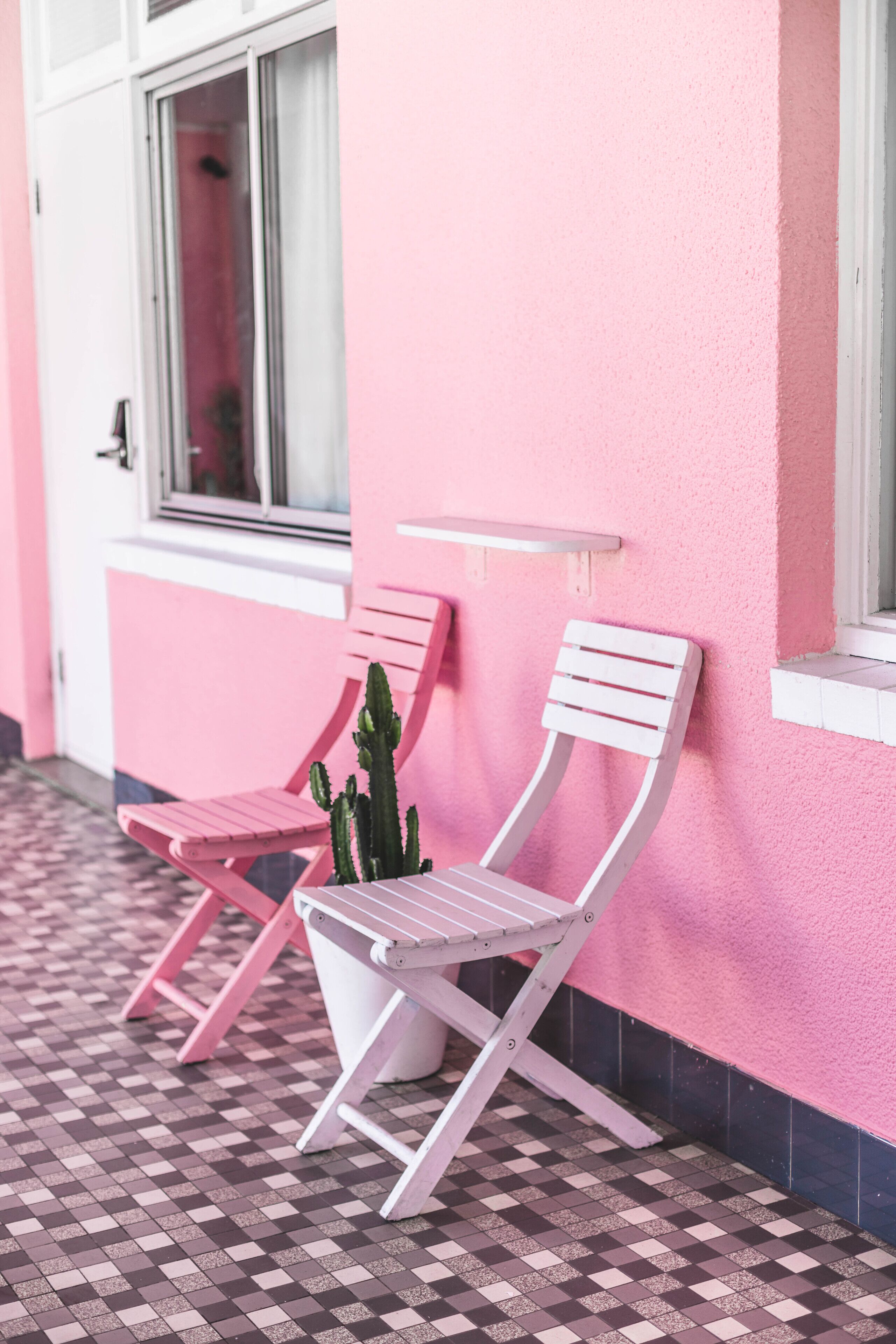 Two white chairs against a pink wall with a window above them.