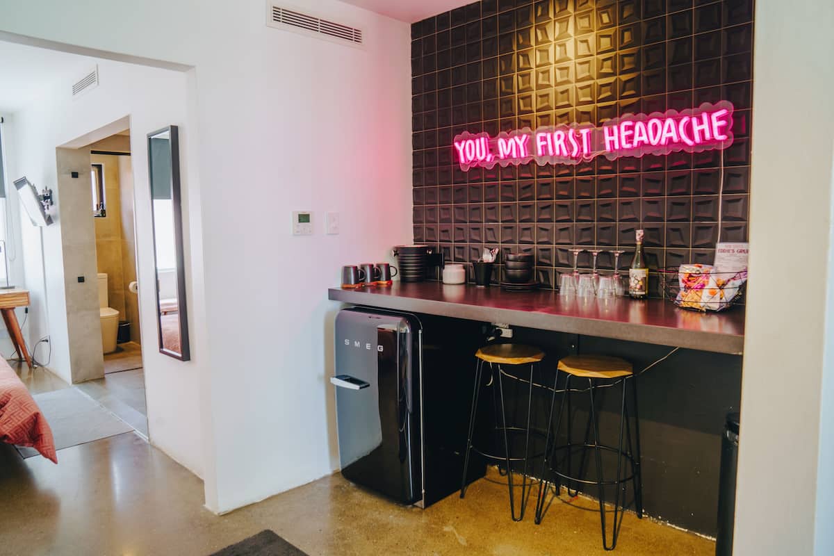 Een compacte keuken met een neonbord, een koelkast en een bar met krukken.