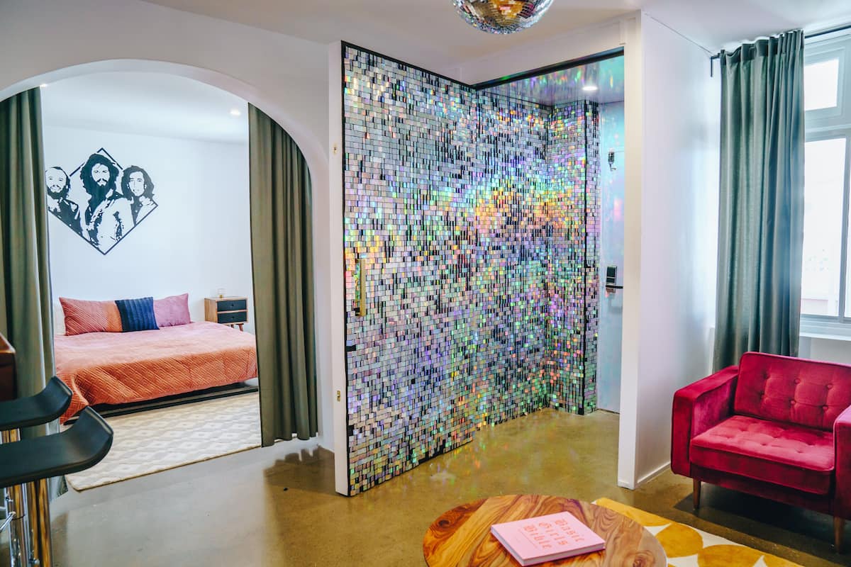 Een moderne hotelkamer met een bed, een rode bank en een wand bekleed met reflecterende tegels.